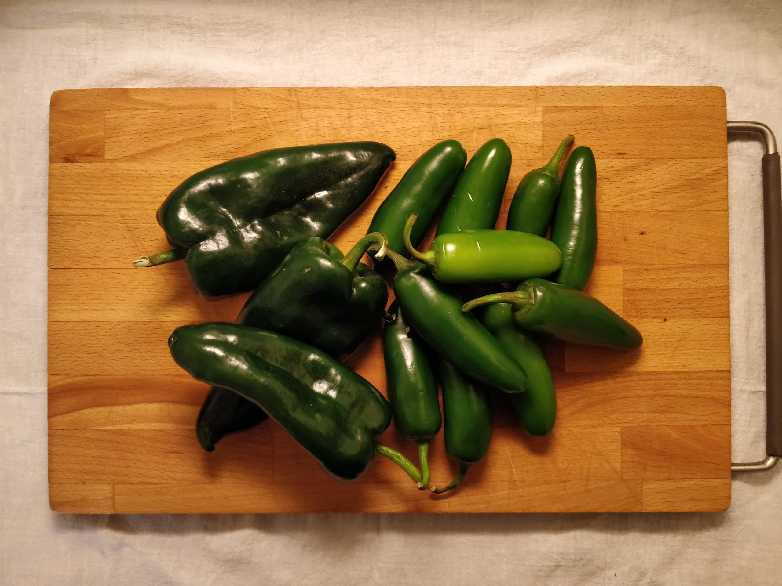 a pile of jalapenos and poblanos on a wooden cutting board