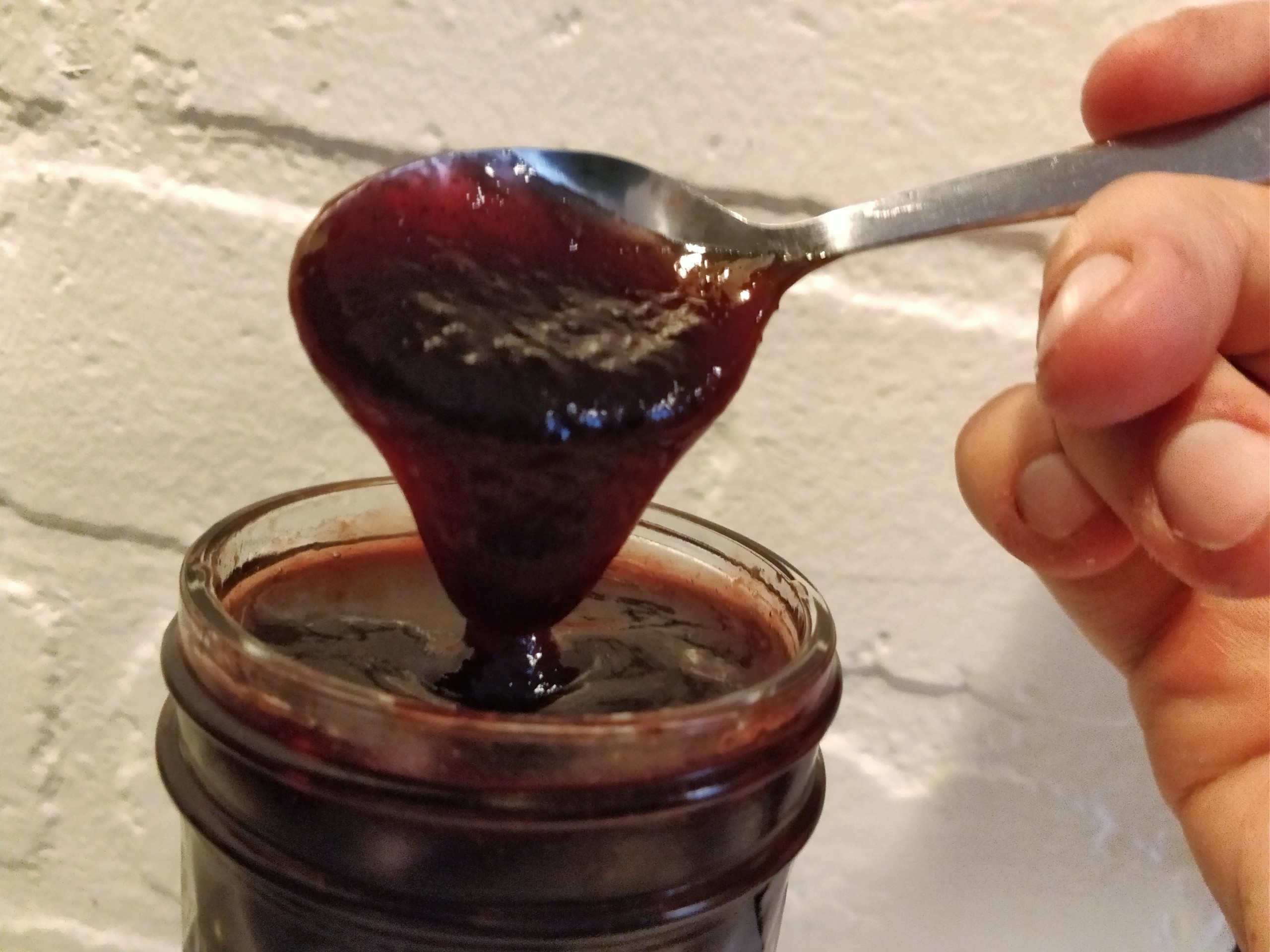 Spoon lifting out of a jar of cherry berry jam showing the thickness of the jam.