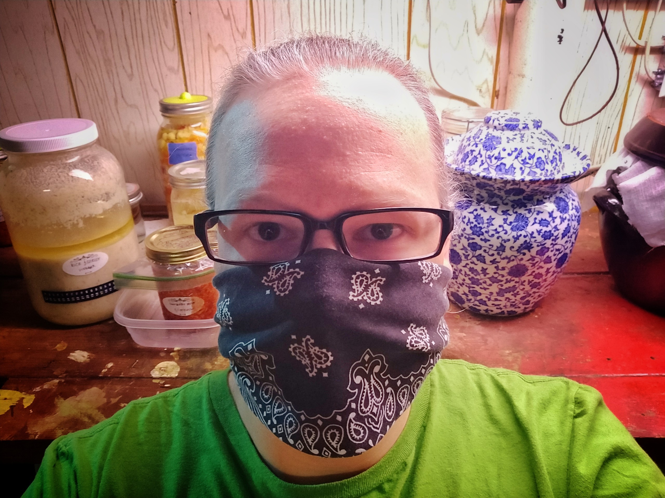 Cory with mask on in front of his shelf of fermentation jars