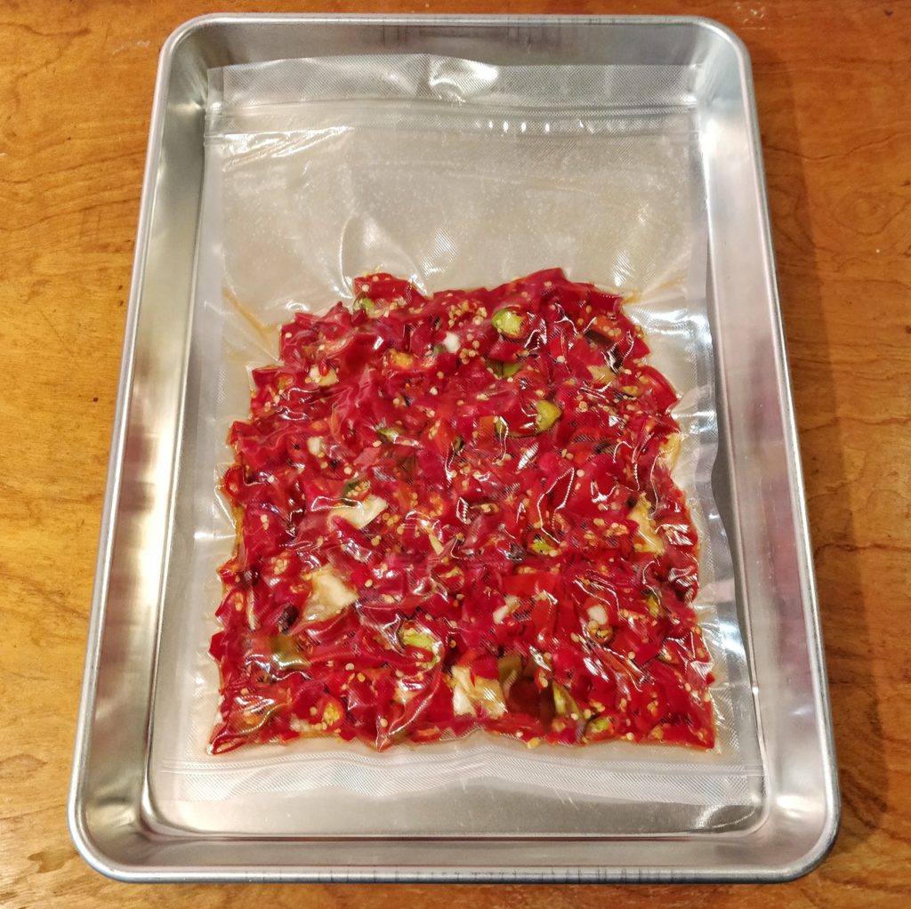 Vacuum-sealed chilies and garlic set in an aluminum pan.