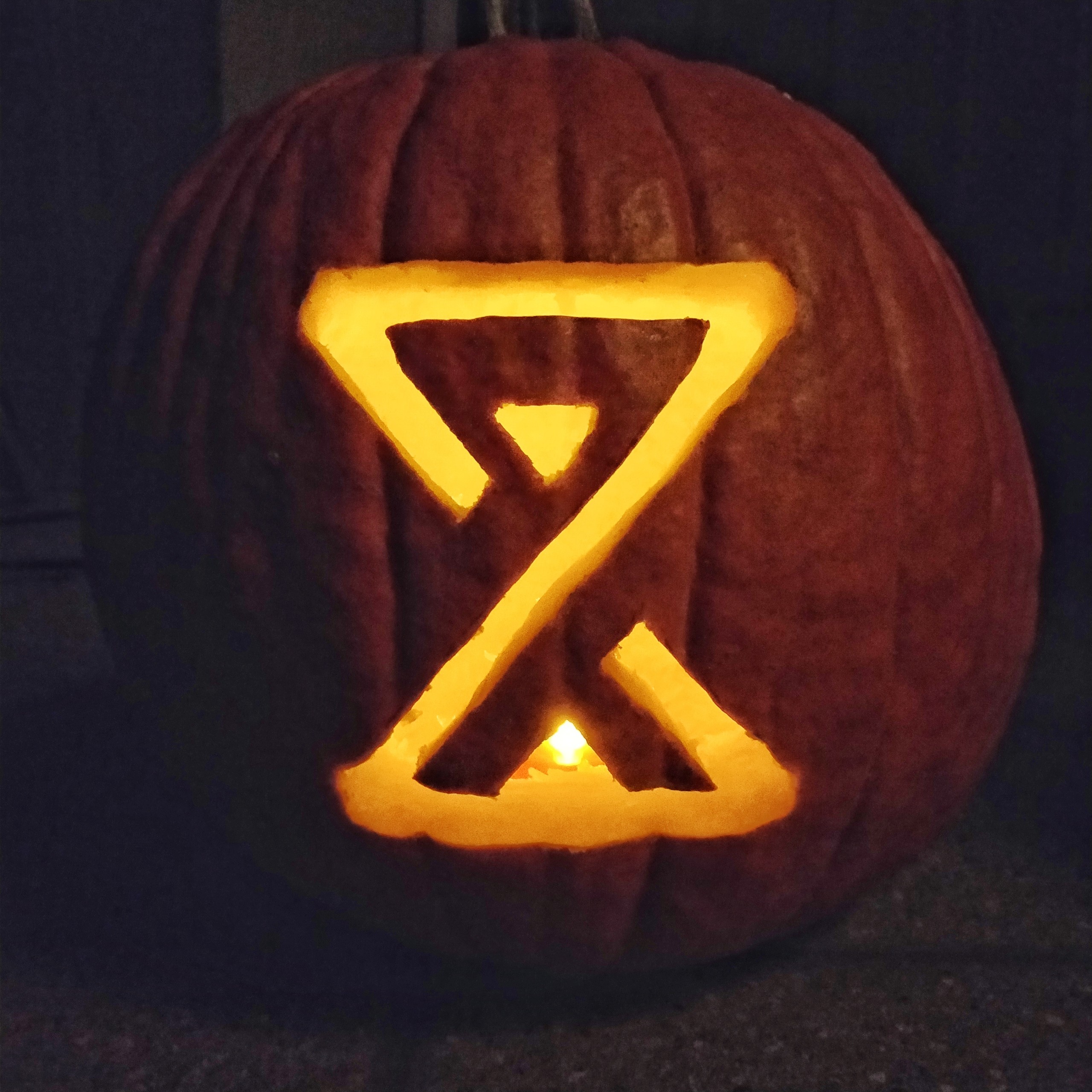 Pumpkin carved with the Crock of Time hourglass symbol, lit from within