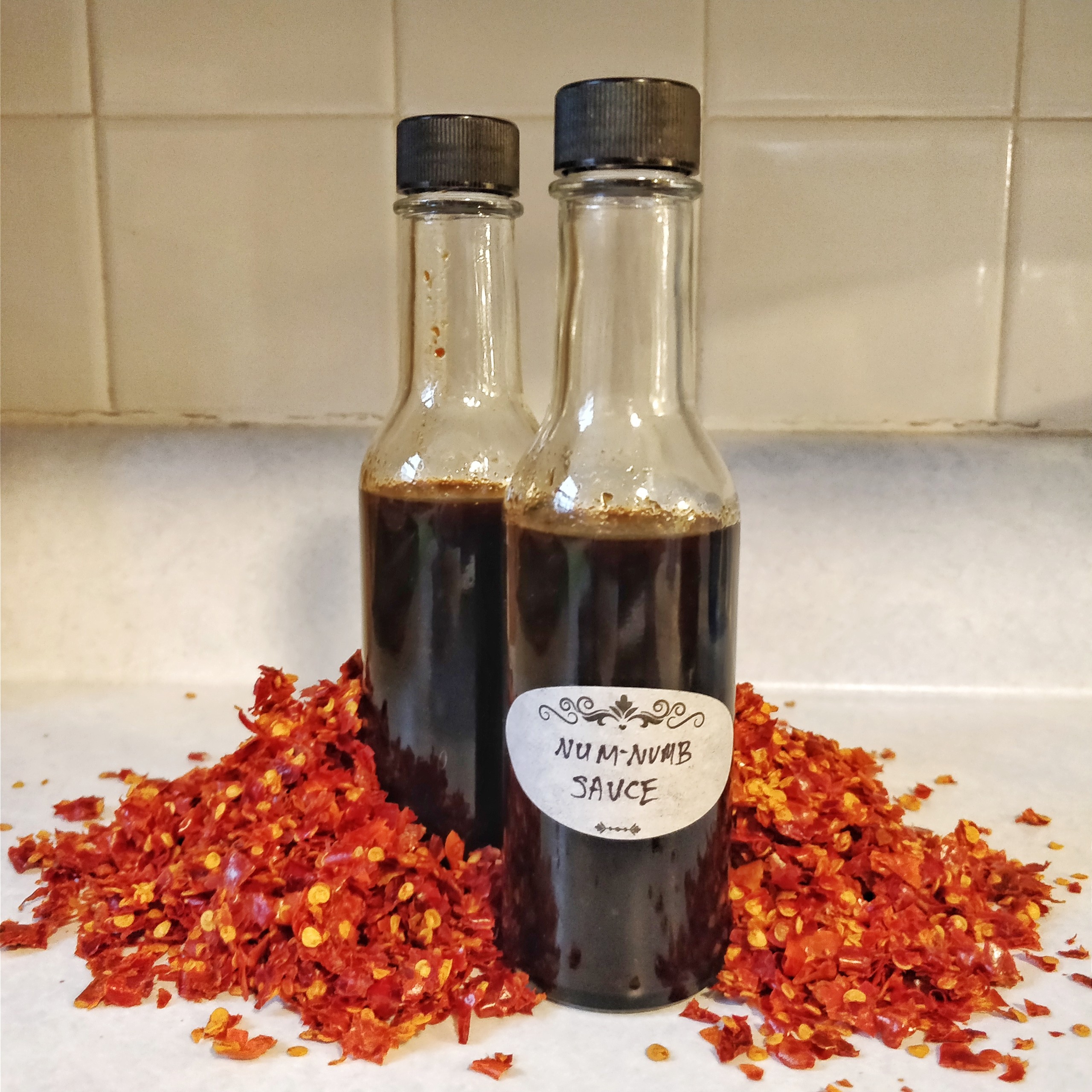 Two bottles of Num-Numb Sauce enveloped in a pile of chili flakes.