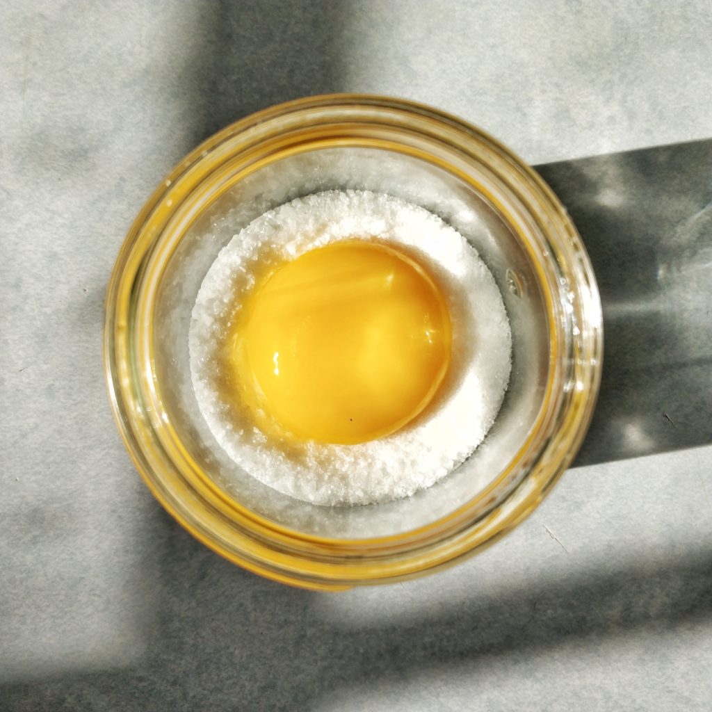 A single egg yolk is nestled in a salt and sugar cure in a small jar