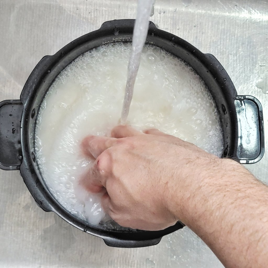 Water is streamed into the bowl of rice while a clawed hand stirs vigorously.
