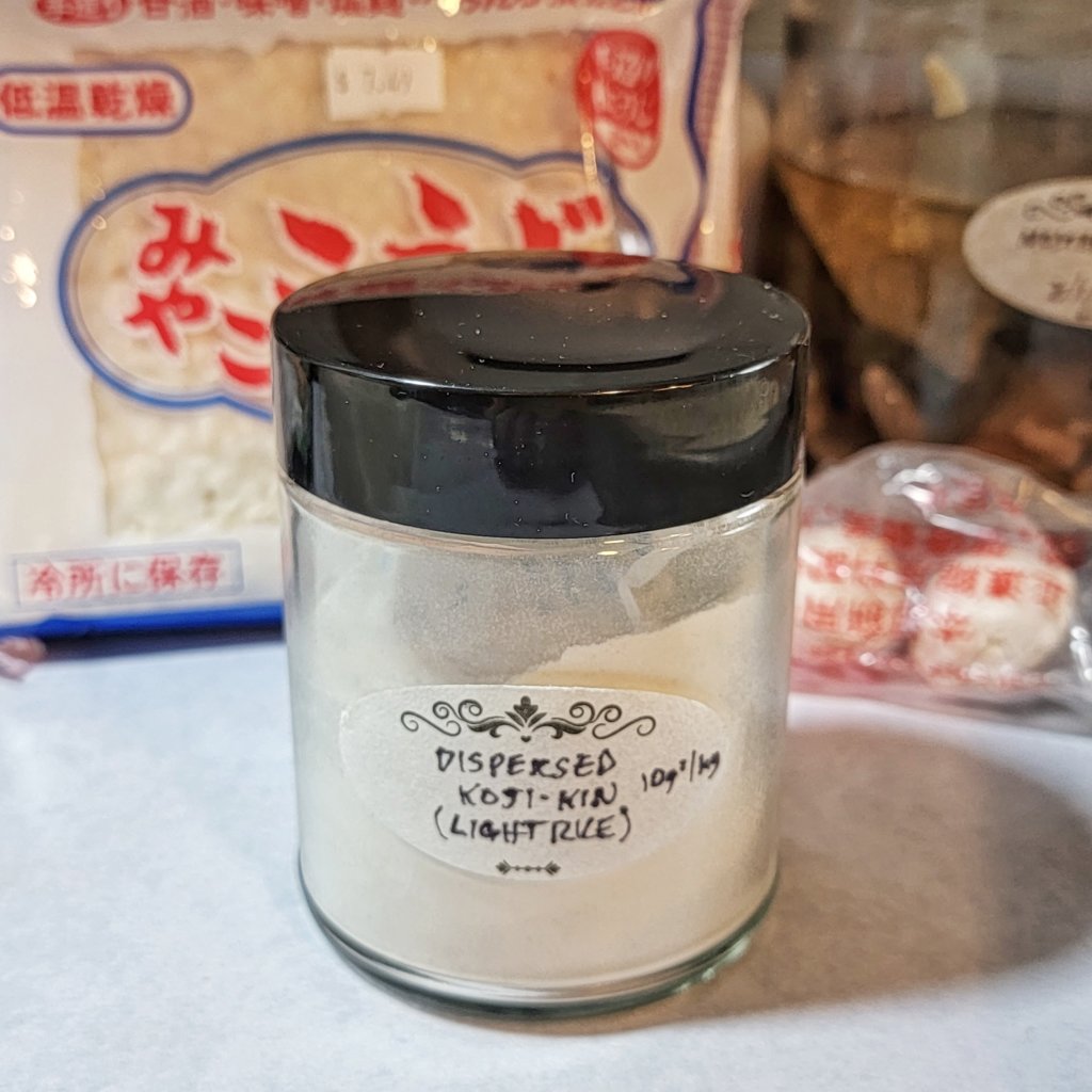 Jar labeled "Koji-kin Dispersed Spores" next to a bag of store-bought dried koji and Chinese qū "yeast balls".