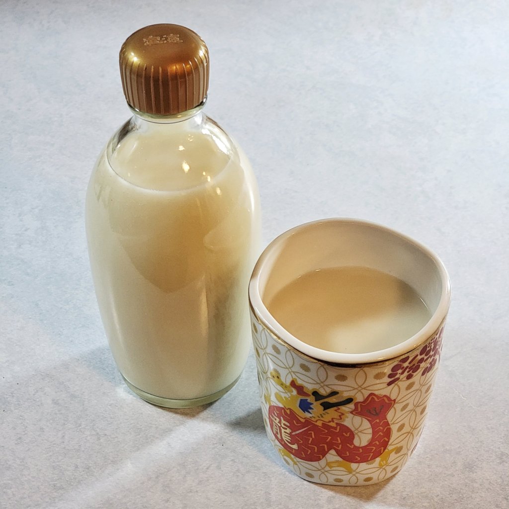 Small glass bottle filled with opaque white liquid next to a cup of the same liquid with a dragon design on it.