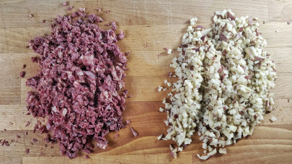 A pile of chopped corned beef next to a pile of finely diced potatoes.
