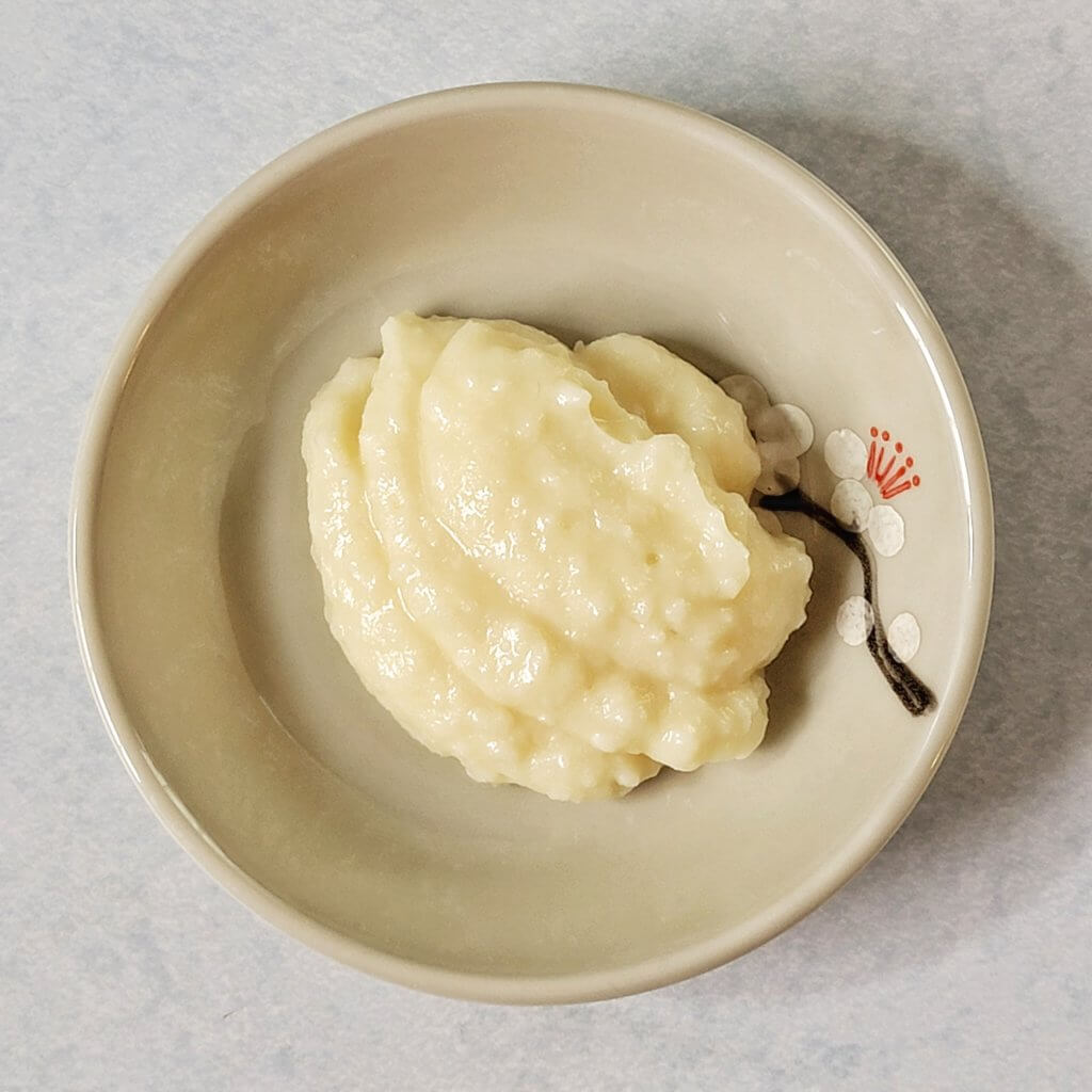 A spoonful of koji ricotta on a small decorative plate. It is smooth and shiny and slightly lumpy.