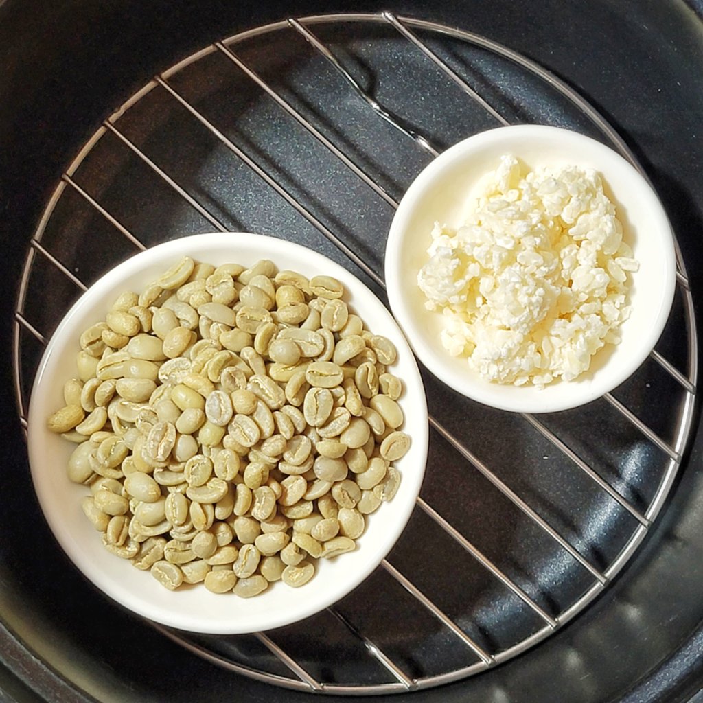 A small plate of green coffee beans and a smaller plate of koji set on a wire rack in a rice cooker.