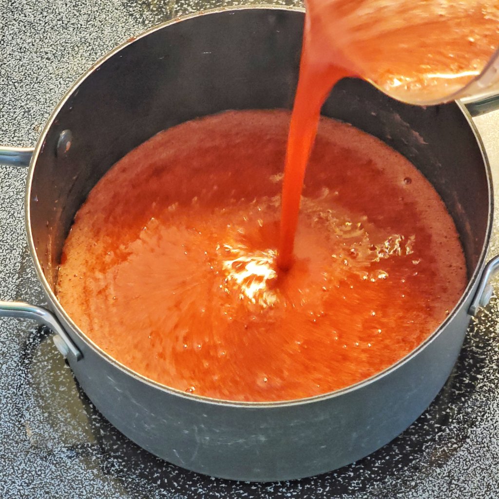 Pouring the smooth strawberry syrup back into a pot.