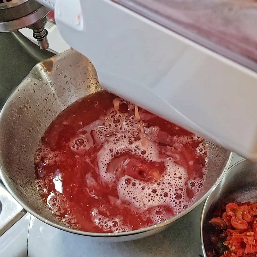 Tomato juice cascading down from mill into a bowl.