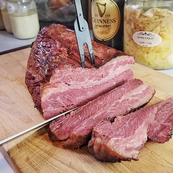 Wagyu corned beef in the process of slicing thick slabs of juicy, pink, super-marbled meat. A bottle of Guinness Extra Stout and a jar of homemade sauerkraut are in the background.