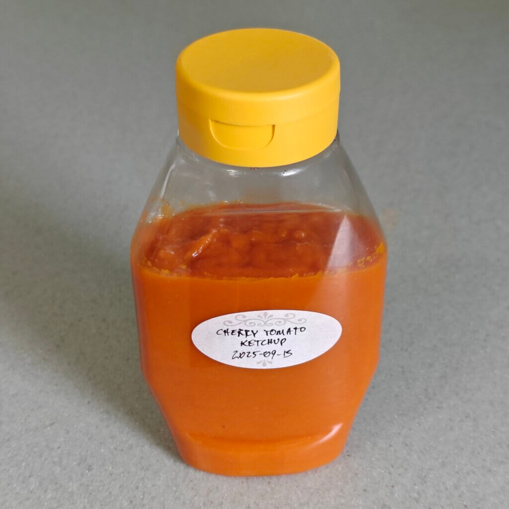 Orange ketchup in a yello-capled squeeze bottle with a hand-written label: "Cherry Tomato Ketchup 2025-09-13".
