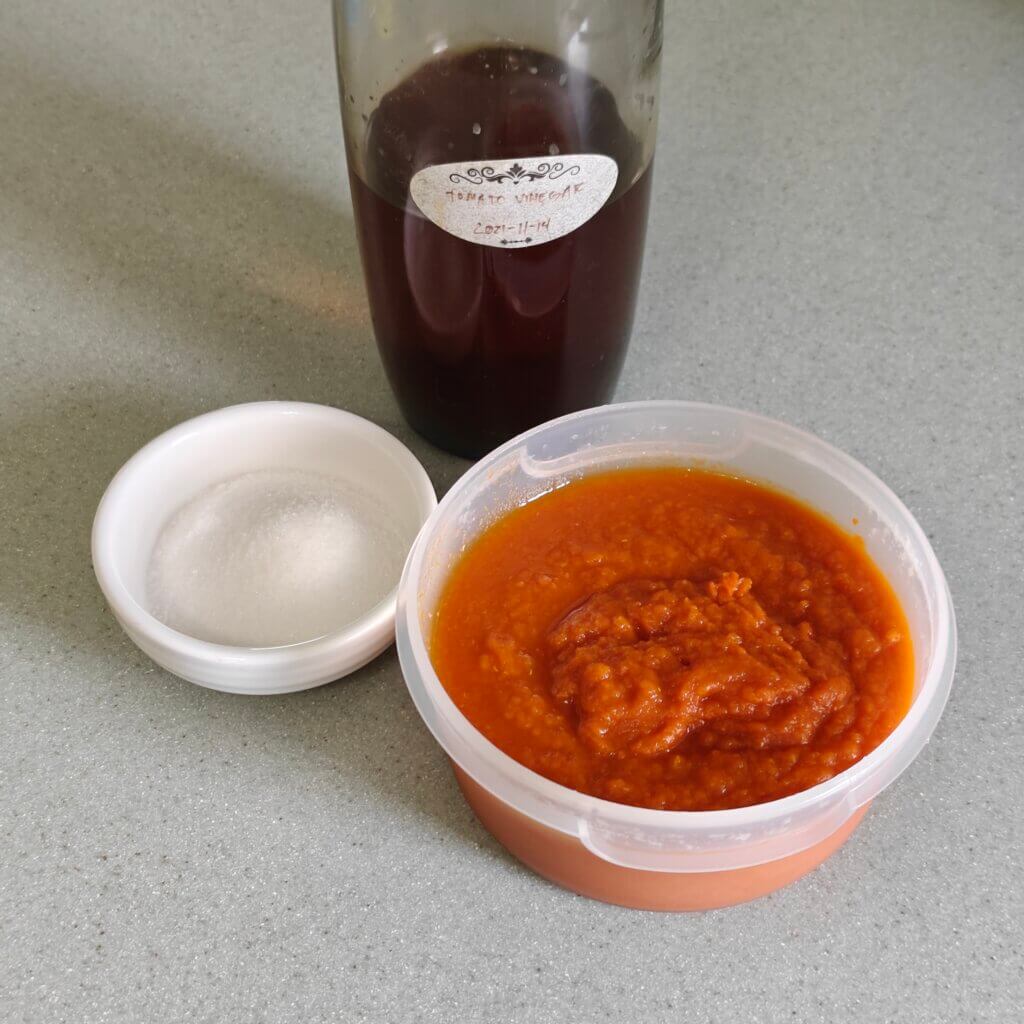Bowl of pulp next to a small bowl of white sugar and a bottle of homemade tomato vinegar.